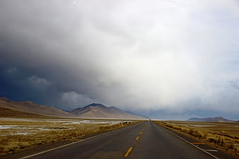 Empty highway stretching through arid landscape under dramatic storm clouds