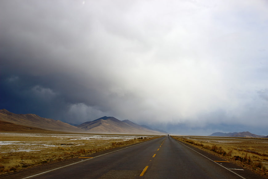 Empty highway stretching through arid landscape under dramatic storm clouds