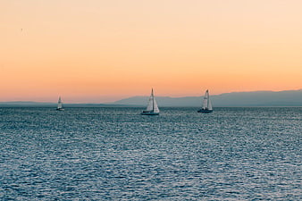 Sailboats on Calm Sea at Sunset with Distant Mountains