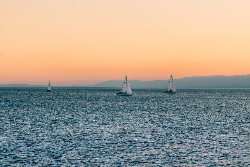 Sailboats on Calm Sea at Sunset with Distant Mountains