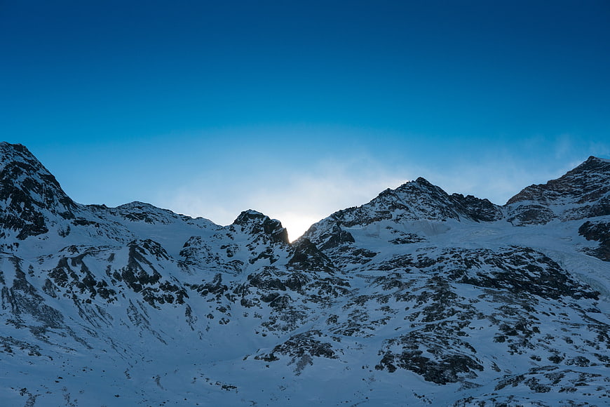 Snowy Mountain Peaks with Sunburst and Blue Sky