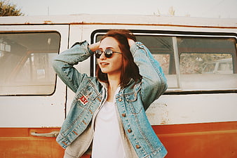 Happy woman in denim jacket and sunglasses leaning against vintage van