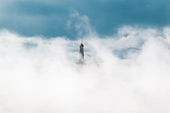 Lighthouse emerging from thick white clouds against blue sky