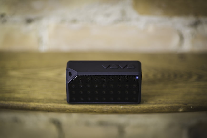 Black portable Bluetooth speaker on wooden shelf