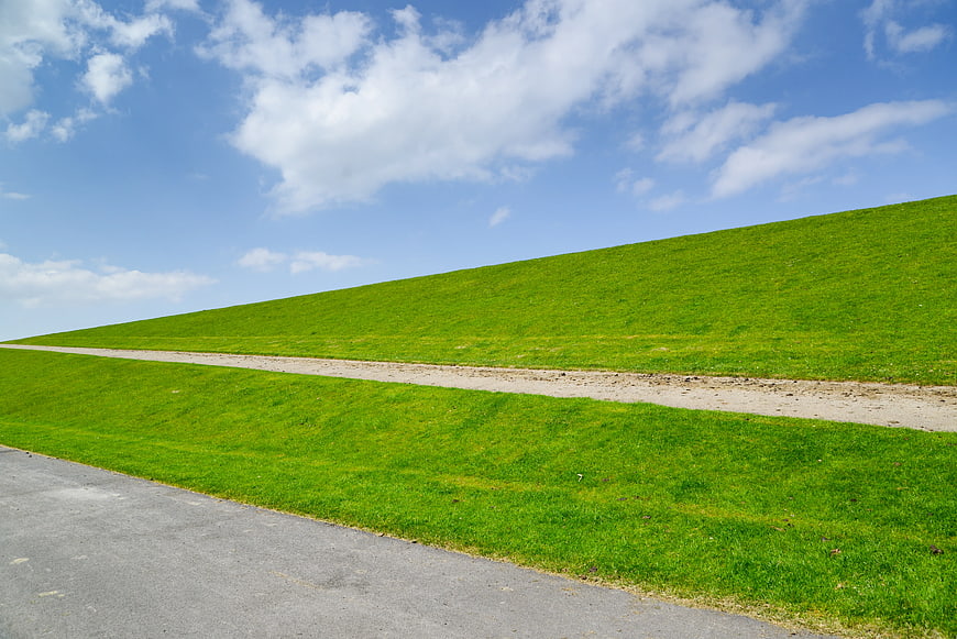 Green grassy hill with dirt path and blue sky