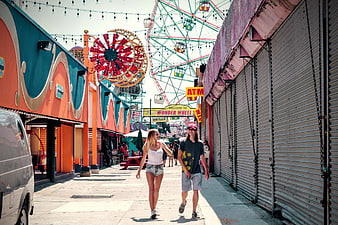 Couple Walking in Amusement Park Alley with Ferris Wheel