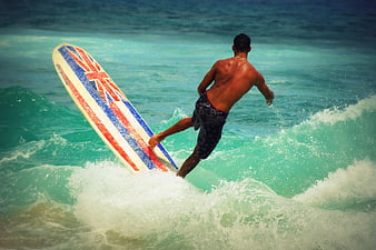 Surfer riding turquoise wave with Union Jack surfboard