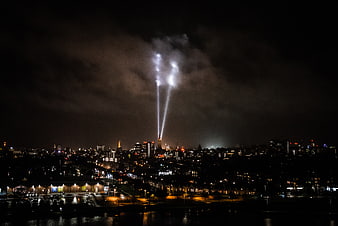 Night cityscape with searchlights illuminating clouds over water