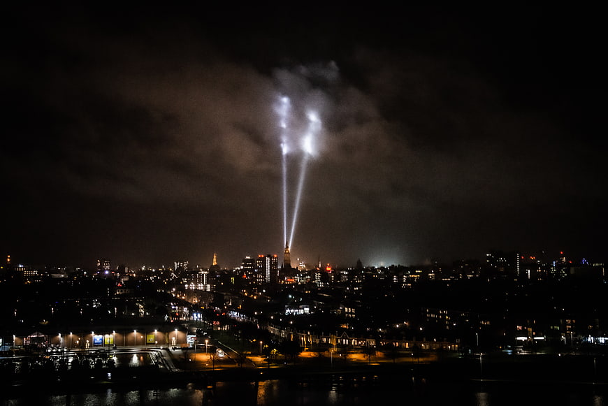 Night cityscape with searchlights illuminating clouds over water