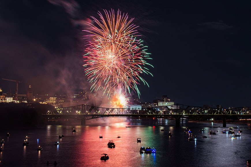 Colorful fireworks exploding over river bridge at night