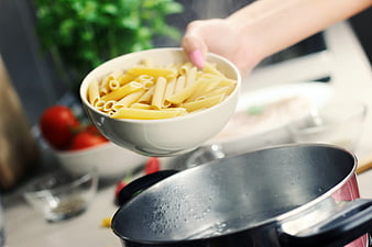 Hand Pouring Penne Pasta into Boiling Pot