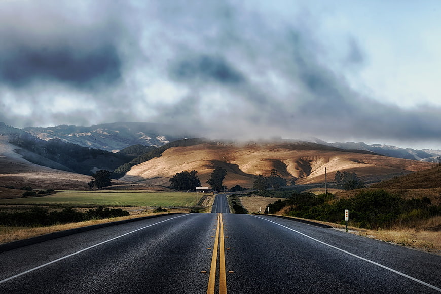 Winding Highway Through Golden Hills Under Dramatic Clouds
