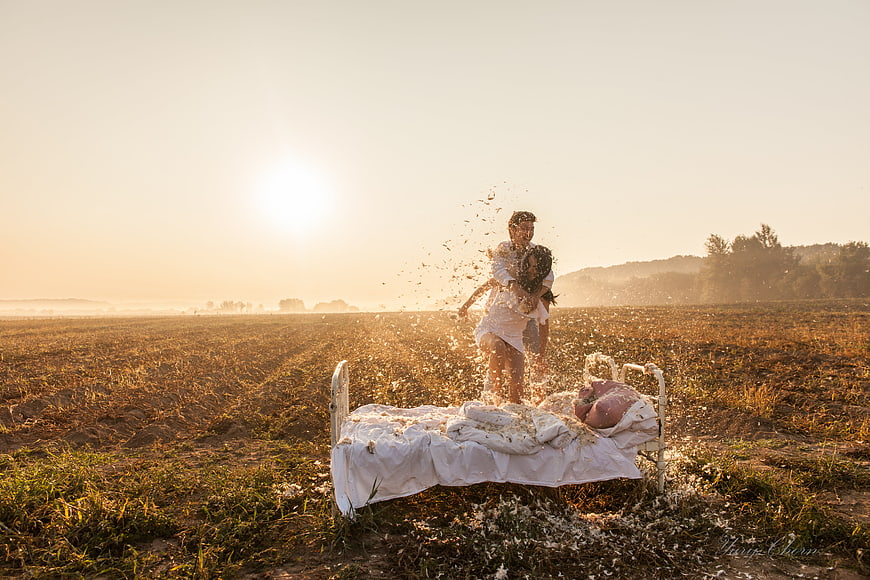Couple embracing in open field with bed and golden hour sunlight