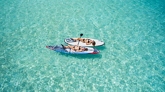 Aerial view of two women relaxing on paddleboards in turquoise water