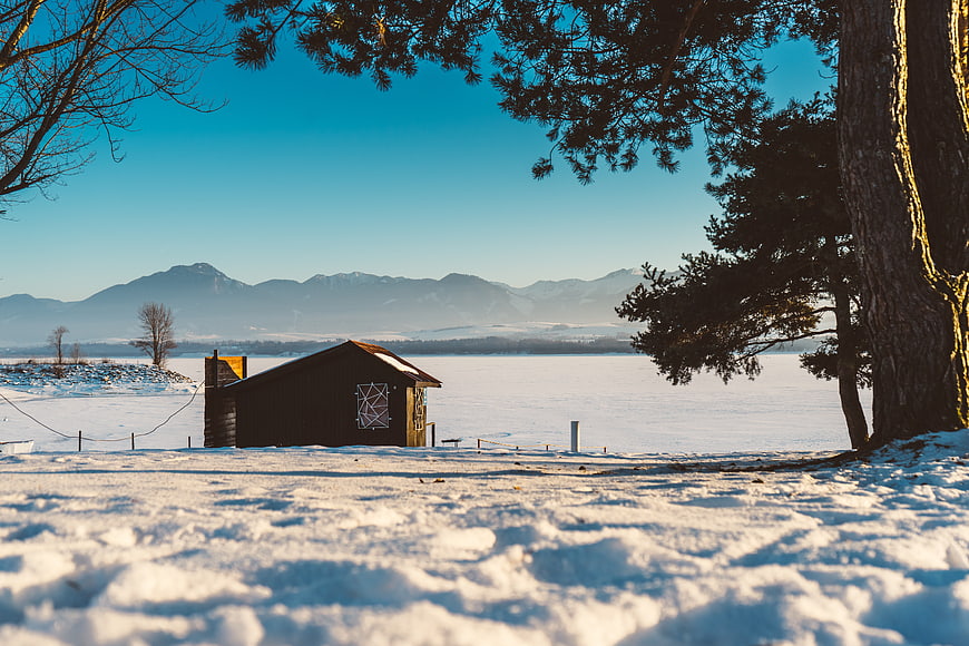 Rustic wooden cabin on frozen lake with mountains
