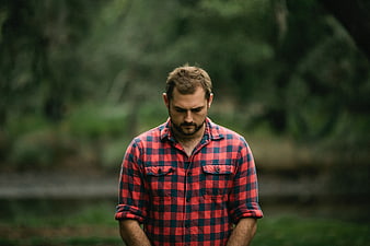 Sad man in red plaid shirt looking down in forest