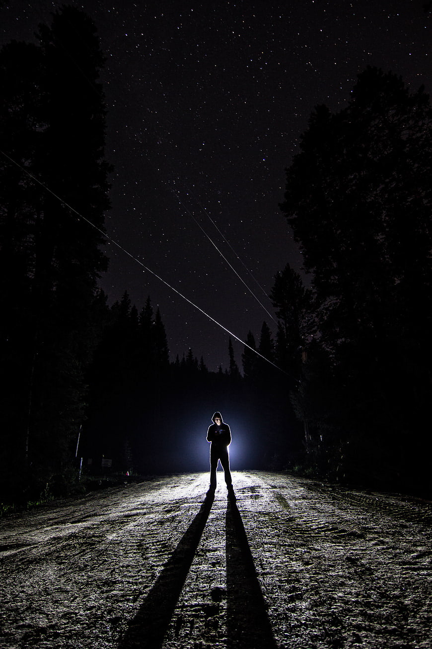 Silhouette of Man Standing on Dark Forest Road Under Starry Sky