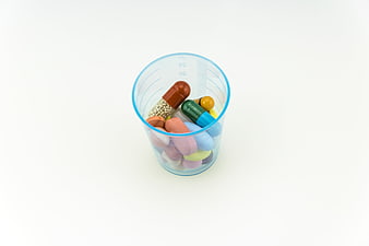 Assorted colorful pills and capsules in a blue measuring cup