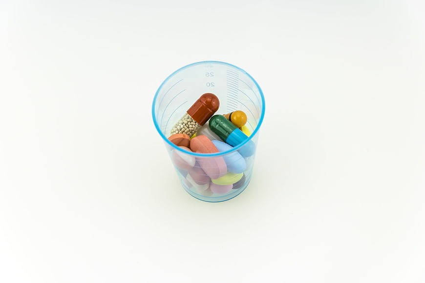 Assorted colorful pills and capsules in a blue measuring cup