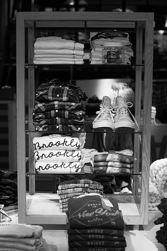Black and white display of folded clothes and sneakers on wooden shelves