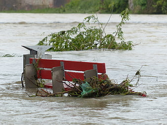 Red park bench submerged in floodwaters with debris