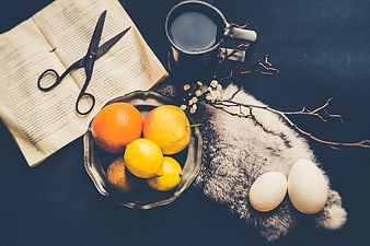 Still life with citrus fruits, eggs, book, and coffee on dark background