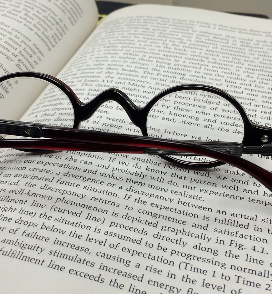 Black Eyeglasses Resting on Open Book Pages