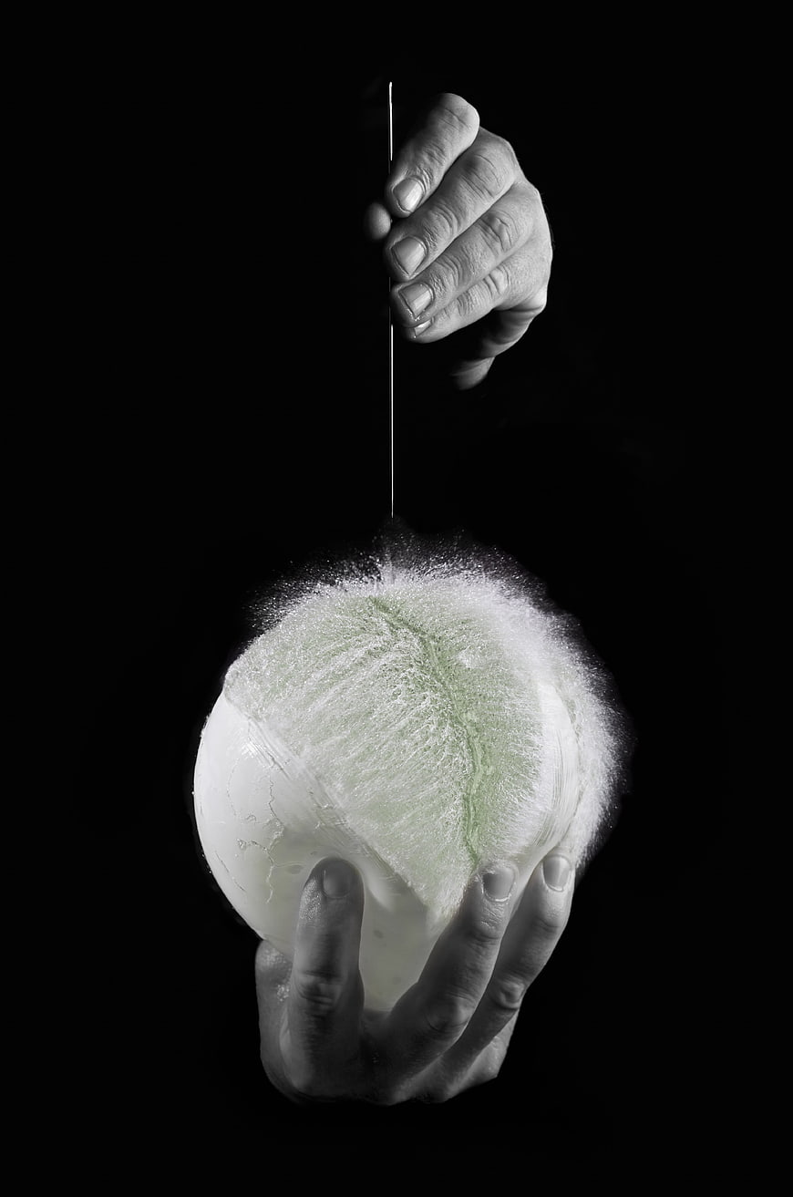Hands Cutting Water Balloon With Knife Against Black Background