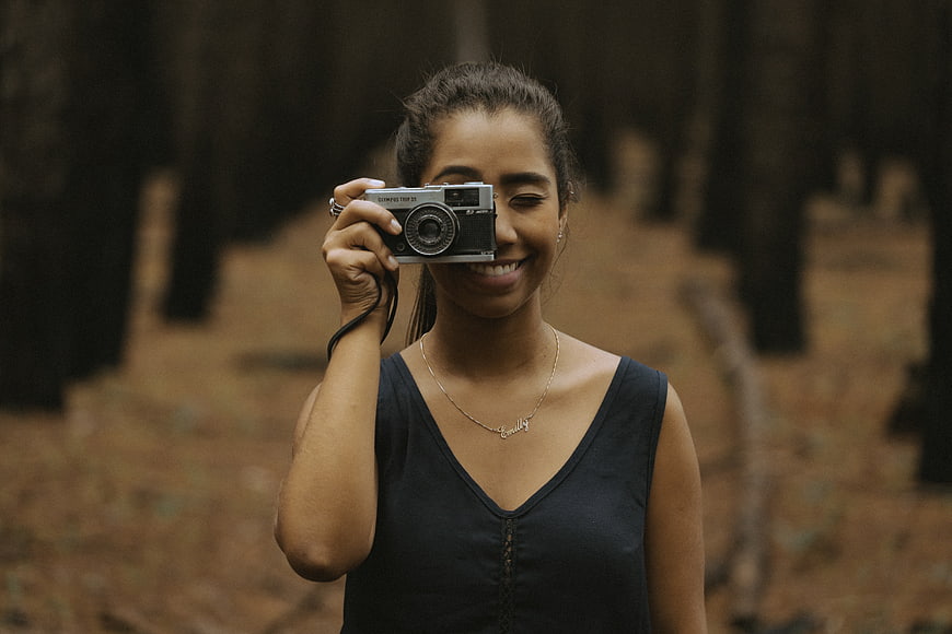 Happy woman holding vintage camera in forest