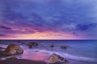 Dramatic purple and pink sunset over rocky ocean beach