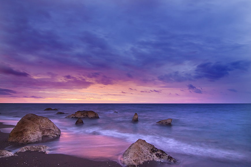 Dramatic purple and pink sunset over rocky ocean beach