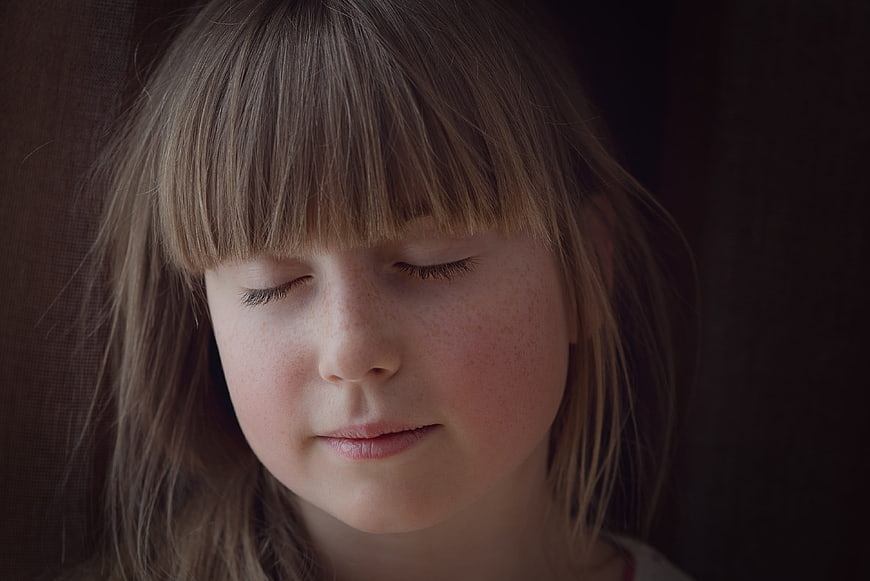 Close-up portrait of a young girl with closed eyes and freckles