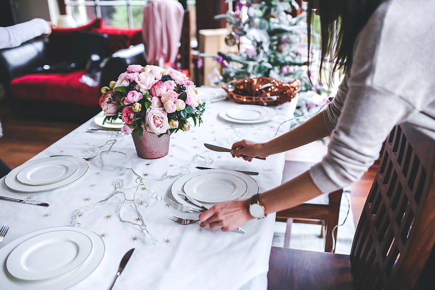 Woman Setting Elegant Christmas Dinner Table with Pink Flowers