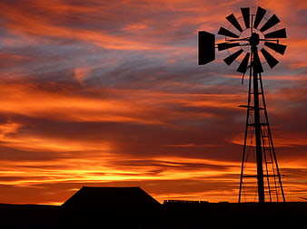 Silhouette of windmill against vibrant orange sunset sky
