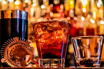 Amber cocktail with ice and bar tools on a wooden counter