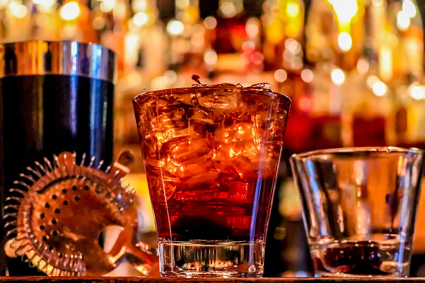 Amber cocktail with ice and bar tools on a wooden counter