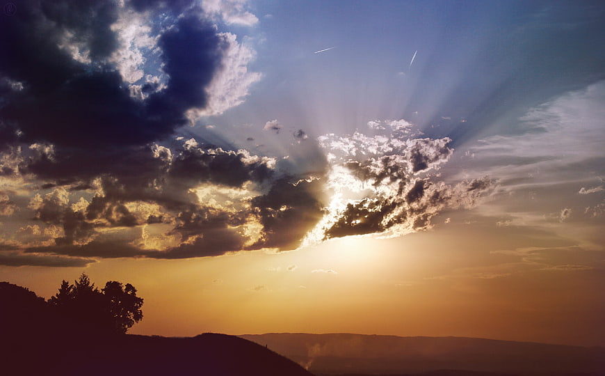 Dramatic sunset with sun rays breaking through clouds over hills