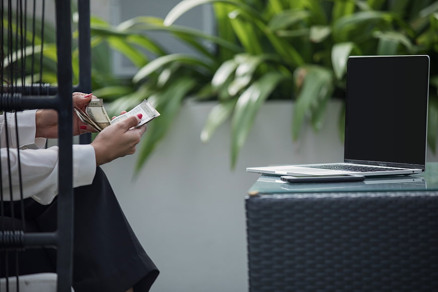 Businesswoman Counting Cash Next to Laptop