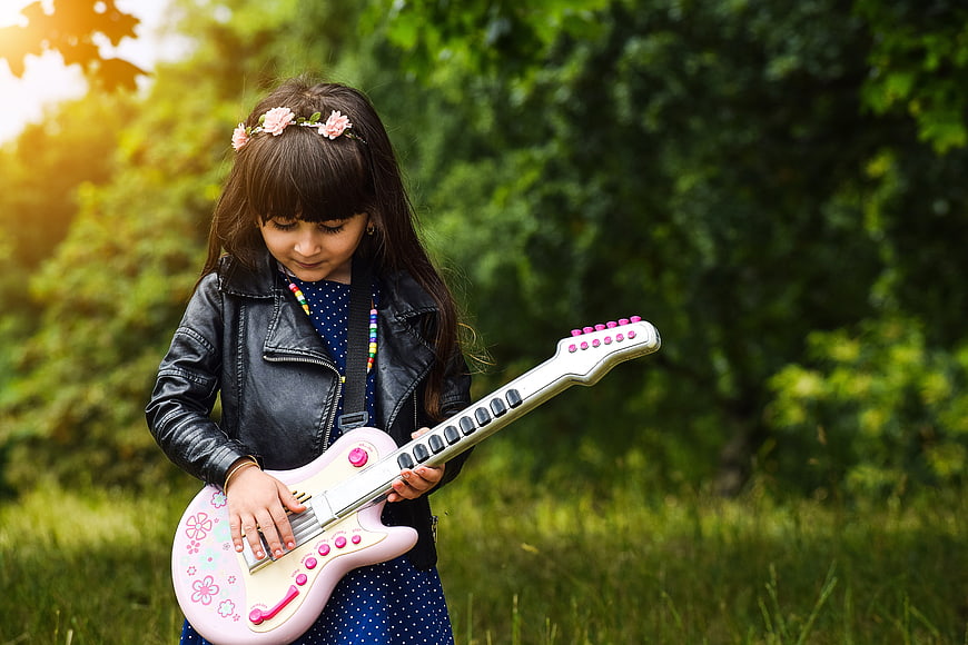 Cute little girl playing pink toy electric guitar outdoors