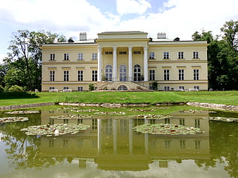 Classical yellow palace with columns reflected in a pond with lily pads