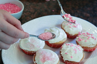Hands Sprinkling Pink Sugar on White Frosted Cupcakes