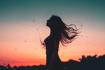 Silhouette of woman with windblown hair against sunset sky