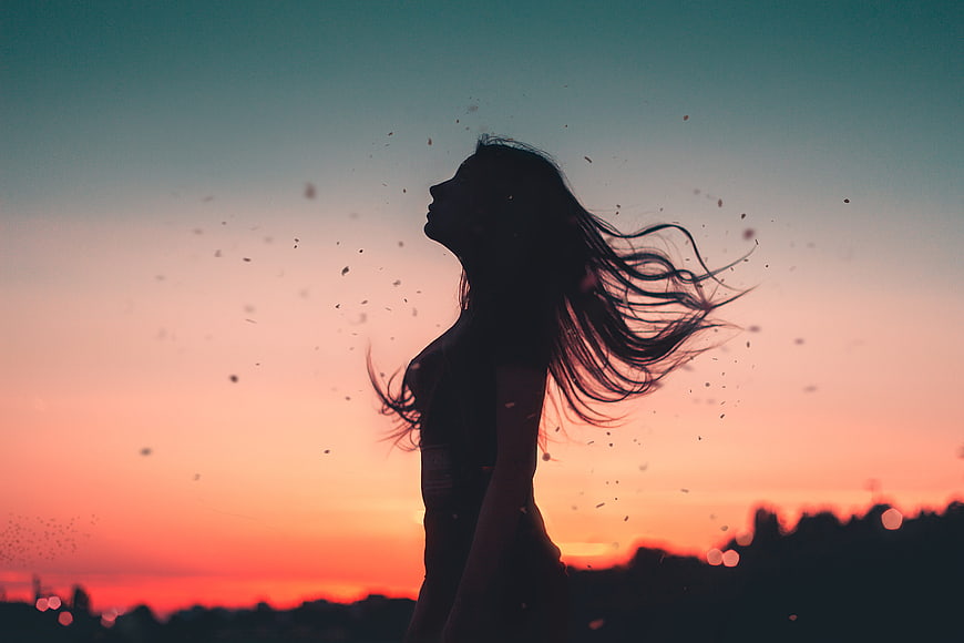 Silhouette of woman with windblown hair against sunset sky