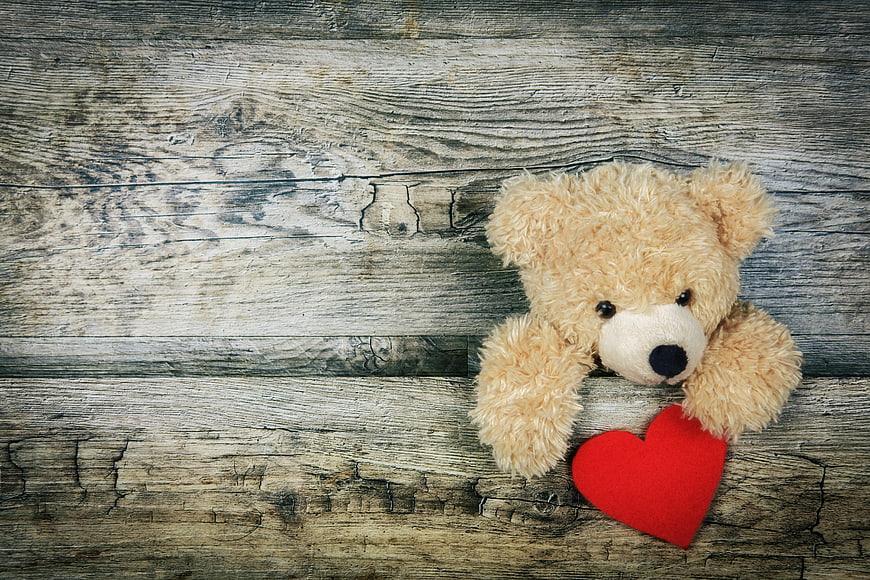 Cute teddy bear with red heart on rustic wood background