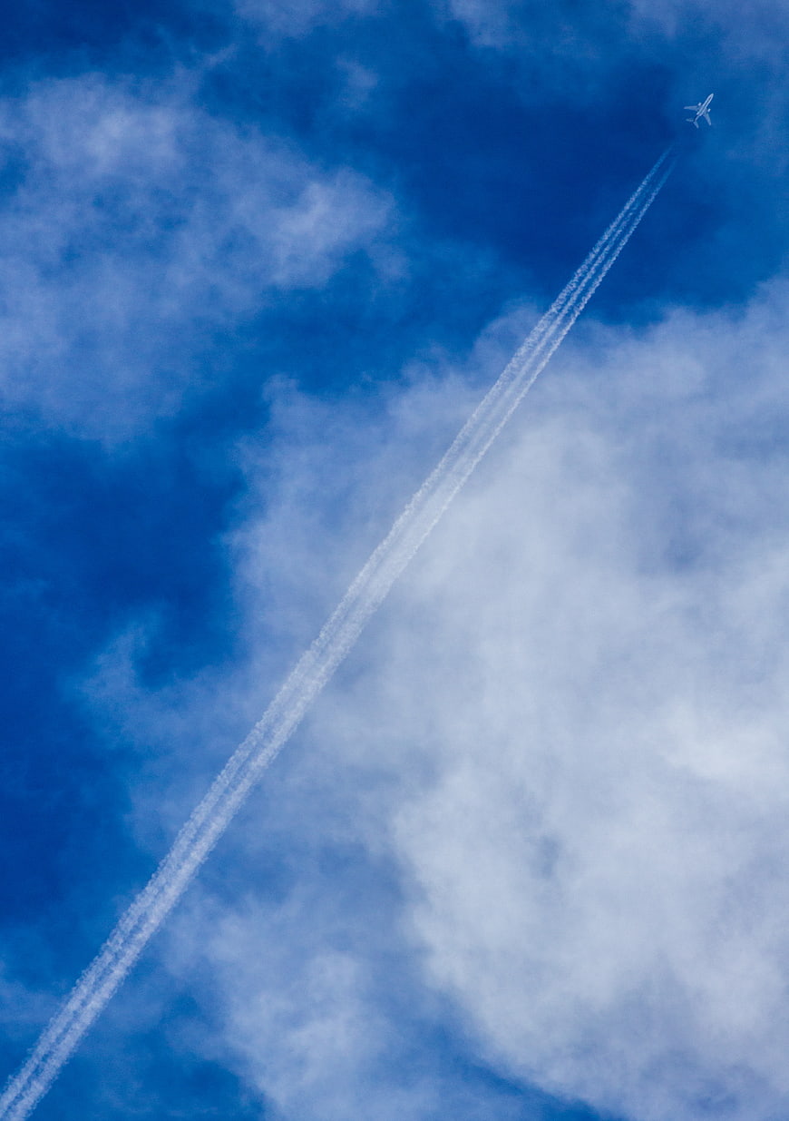 Airplane with contrails flying through blue sky with clouds