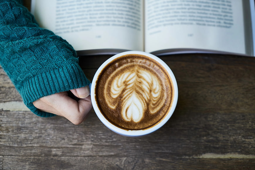 Overhead view of latte art coffee cup with open book