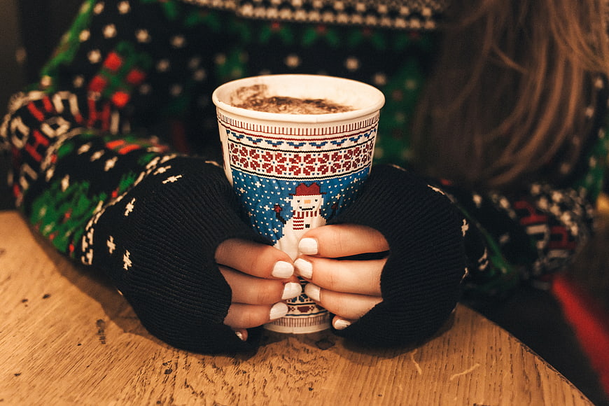 Woman holding festive Christmas coffee cup in cozy sweater