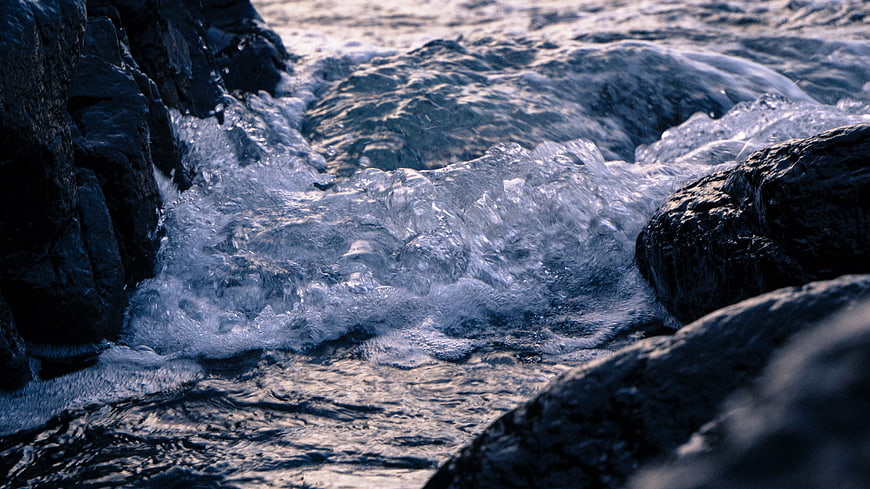 Close-up of turbulent ocean waves crashing against dark rocks