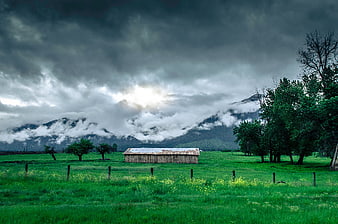 Dramatic storm clouds over a rustic wooden cabin in a green meadow