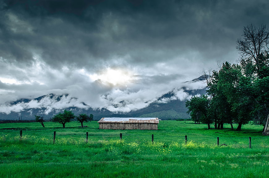 Dramatic storm clouds over a rustic wooden cabin in a green meadow